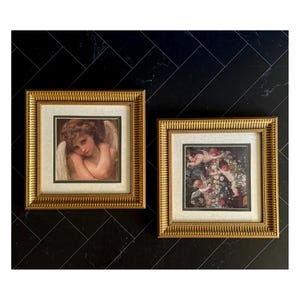 May include: Two square framed prints featuring classical art. The left print shows a single winged figure with curly hair. The right print depicts three winged figures amidst a dense floral arrangement. Both are encased in ornate gold frames.