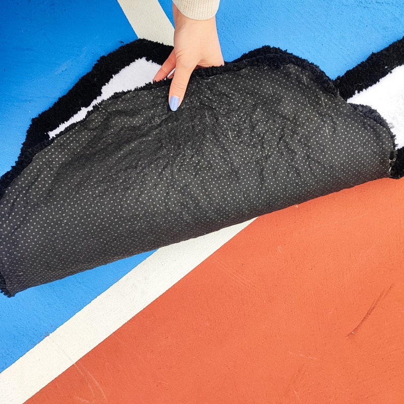 May include: A black and white fluffy rug with a black rubber backing. The rug is folded in half and the backing is visible.