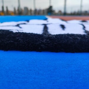 May include: Close-up of a blue and black rug with a white design. The rug has a fuzzy texture and is made of different materials.