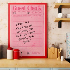 Peut inclure: Un ch&egrave;que de restaurant encadr&eacute; rose avec une citation motivationnelle manuscrite : "ne laissez jamais la peur de frapper un home run vous emp&ecirc;cher de jouer le jeu".