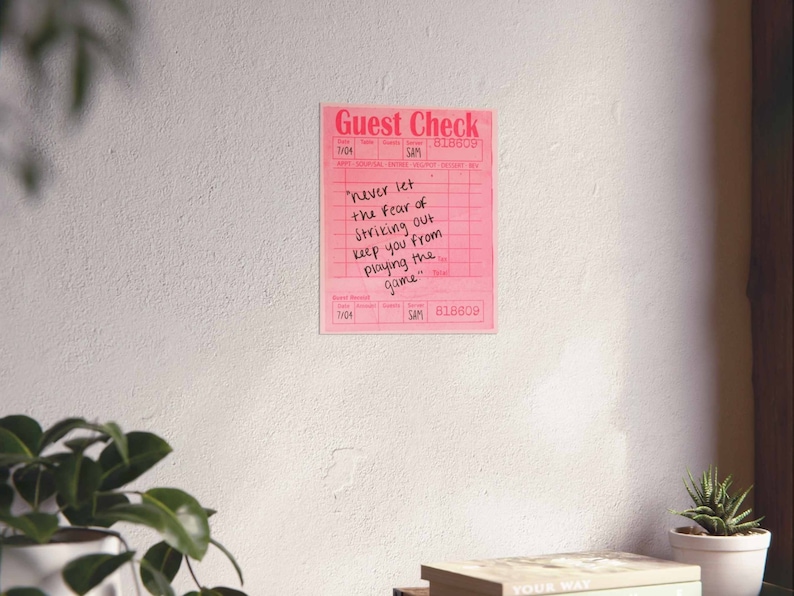 Peut inclure: Un ch&egrave;que de restaurant rose avec la citation "Ne laissez jamais la peur de frapper un home run vous emp&ecirc;cher de jouer le jeu." &eacute;crite &agrave; l'encre noire.