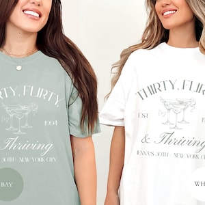 May include: Two t-shirts with the text "Thirty, flirty, est 1994 & Thriving" and a graphic of three martini glasses. The text "Jenna's 30th - New York City" is also included. One shirt is a light green color and the other is white.