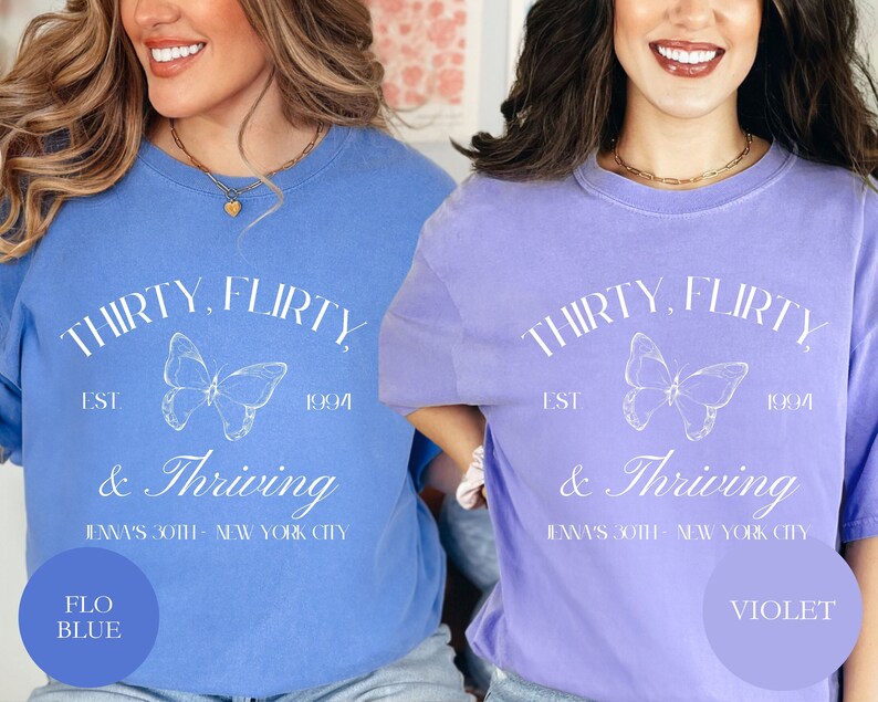 May include: Two t-shirts with a butterfly graphic and the text "Thirty, flirty & thriving" in white. The shirt on the left is blue and the shirt on the right is purple. The text "Flo Blue" is in a circle on the left shirt and the text "Violet" is in a circle on the right shirt.