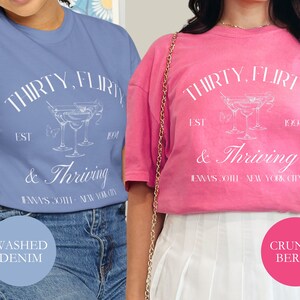 May include: Two women wearing t-shirts with the text "Thirty, flirty & thriving" and a graphic of a cocktail glass. The text also includes "Est. 1994" and "Jenna's 30th - New York City". One shirt is blue and the other is pink.