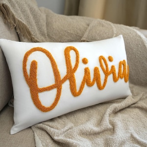 a white pillow with an orange embroidered name on it