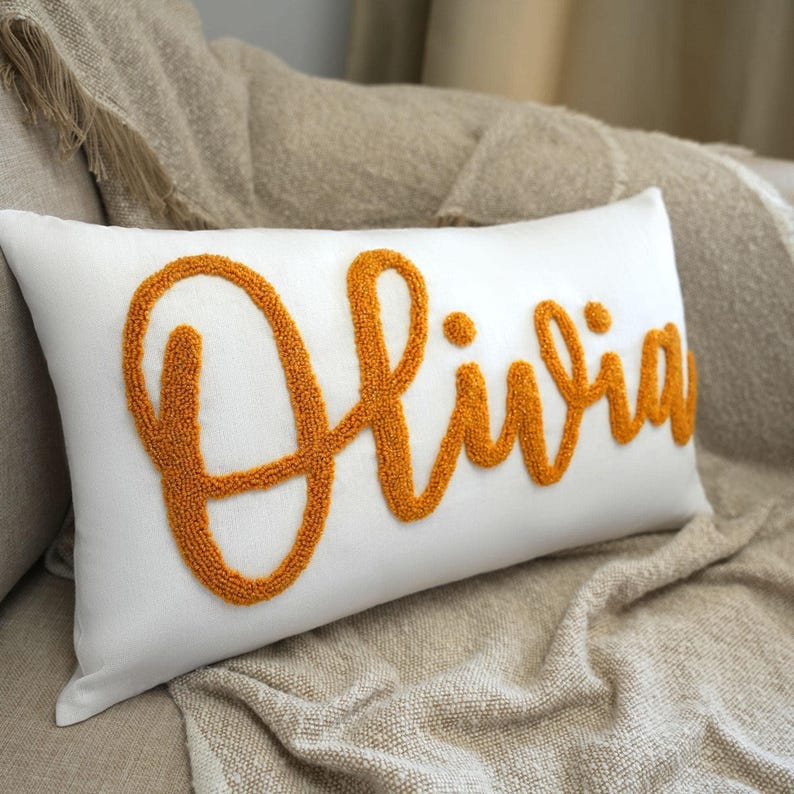 a white pillow with an orange embroidered name on it