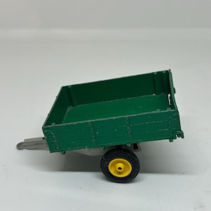 May include: A green toy trailer with a single yellow wheel. The trailer has a flatbed with wooden sides.