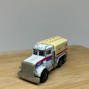 May include: White toy truck with a yellow tanker trailer. The truck has a red and blue stripe on the side and the words "Sunoco" on the door. The tanker trailer has the words "Sunoco" on the side.