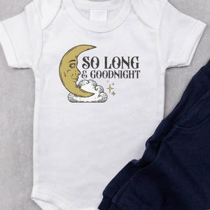 May include: A white baby bodysuit and navy blue sweatpants set. The bodysuit features a smiling crescent moon graphic with the text "SO LONG & GOODNIGHT". The set is designed for infants and toddlers.