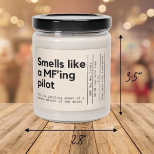 May include: A white soy wax candle with a black lid and label that reads "Smells like a MF'ing pilot" and "The invigorating scent of a badass master of the skies". The candle is 8.9 cm tall and 7.1 cm wide.