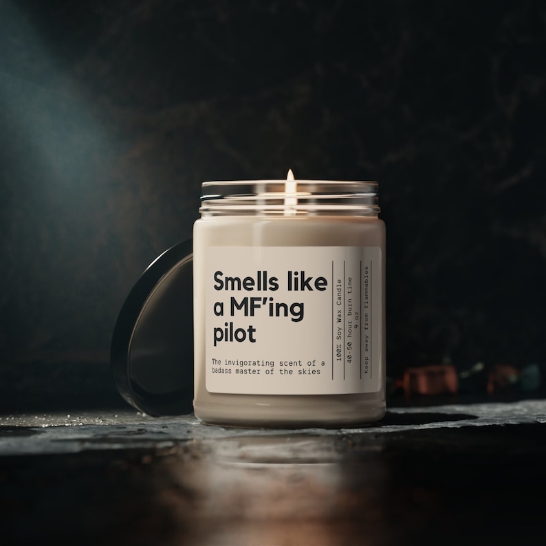 May include: A beige soy wax candle with a black label that reads "Smells like a MF'ing pilot" and "The invigorating scent of a badass master of the skies". The candle is 100% soy wax and has a 40-50 hour burn time.