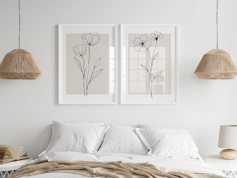 May include: Two framed floral art prints. Each print features a delicate black line drawing of flowers on a neutral background. The artwork is displayed above a bed with white linens, creating a serene and minimalist aesthetic.