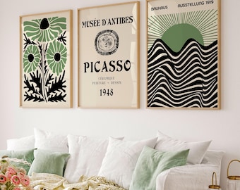 May include: Three framed art prints with a mid-century modern aesthetic. The prints feature botanical and abstract designs in green, black, and beige. One print displays the text "MUSÉE D'ANTIBES PICASSO 1948". Another print has the text "BAUHAUS AUSSTELLUNG 1919".