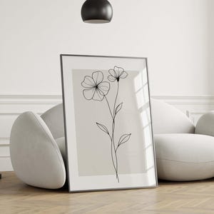 May include: Framed floral art print featuring a minimalist line drawing of two flowers and leaves on a neutral background. The black lines contrast against the light beige, creating a modern aesthetic. The artwork is displayed in a black frame.