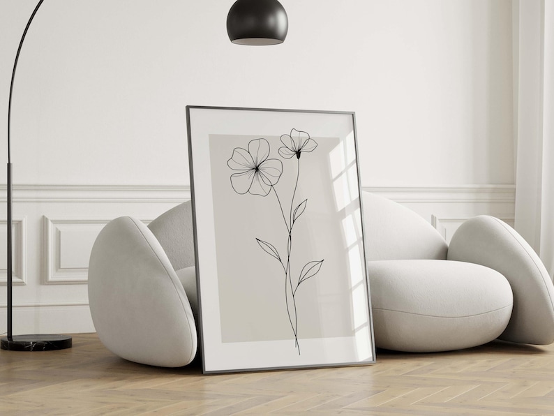 May include: Framed floral art print featuring a minimalist line drawing of two flowers and leaves on a neutral background. The black lines contrast against the light beige, creating a modern aesthetic. The artwork is displayed in a black frame.