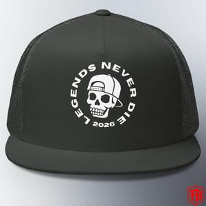 May include: Black trucker hat with a white graphic of a skull wearing a backwards baseball cap. The text "LEGENDS NEVER DIE 2026" is in a circle around the skull. The hat has a mesh back and a curved brim.