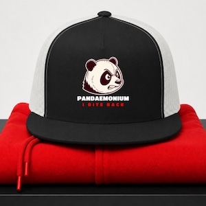 May include: Black and white trucker hat with a panda illustration and the text "PANDAEMONIUM I BITE BACK". The hat has a black brim and a white mesh back, resting on a red hoodie.