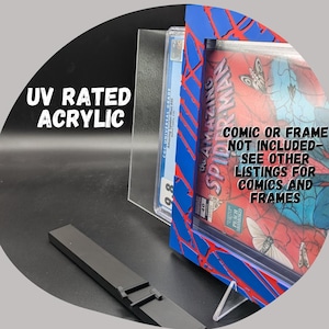 Puede incluir: Un marco de cómic de acrílico azul y rojo con un diseño de telaraña. El marco está clasificado UV y viene con un soporte de acrílico transparente. El texto "The Amazing Spider-Man" es visible en el cómic dentro del marco.  "Comic or frame not included - see other listings for comics and frames" también es visible en la imagen.
