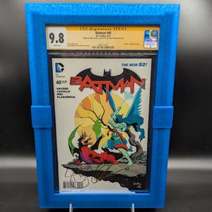 Puede incluir: Un cómic calificado en una caja protectora azul. El cómic es Batman #40, parte de la serie The New 52. La portada presenta una ilustración colorida de Batman luchando contra una criatura alada. El cómic está calificado con 9.8 por CGC.
