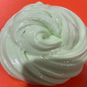 May include: A close-up of a light green slime with a glossy finish. The slime is in a swirl pattern and appears to be very soft and smooth.