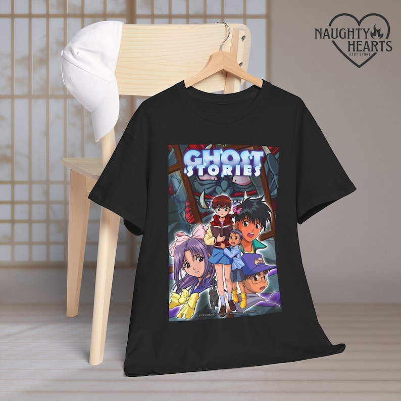 May include: Black t-shirt with a graphic print of the anime Ghost Stories. The graphic features a group of characters from the show, including a girl with purple hair and a boy with brown hair. The text "Ghost Stories" is printed in blue letters.