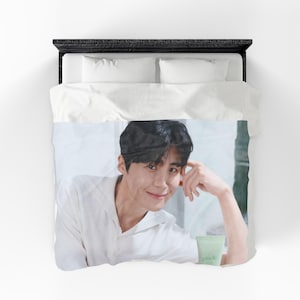 May include: A white duvet cover featuring a smiling person in a white shirt. The person is resting their head on their hand. A light green tube of product with the word "micle" is visible.