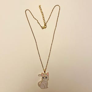 Op de afbeelding: Een gouden ketting met een witte emaille kattenhanger. De kat heeft roze oren en een gouden halve maan op zijn voorhoofd.