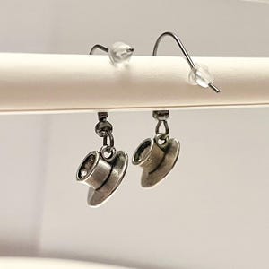 Könnte beinhalten: Ein Paar silberfarbene Ohrringe mit einem kleinen Teetassen-Anhänger, der an jedem Ohrring hängt.