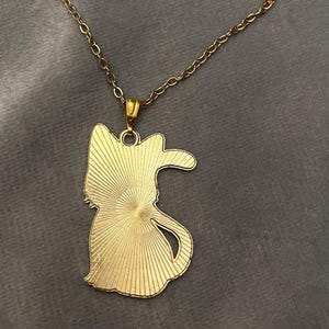 Op de afbeelding: Een gouden ketting met een hanger in de vorm van een kat. De hanger heeft een zonnestralenontwerp.