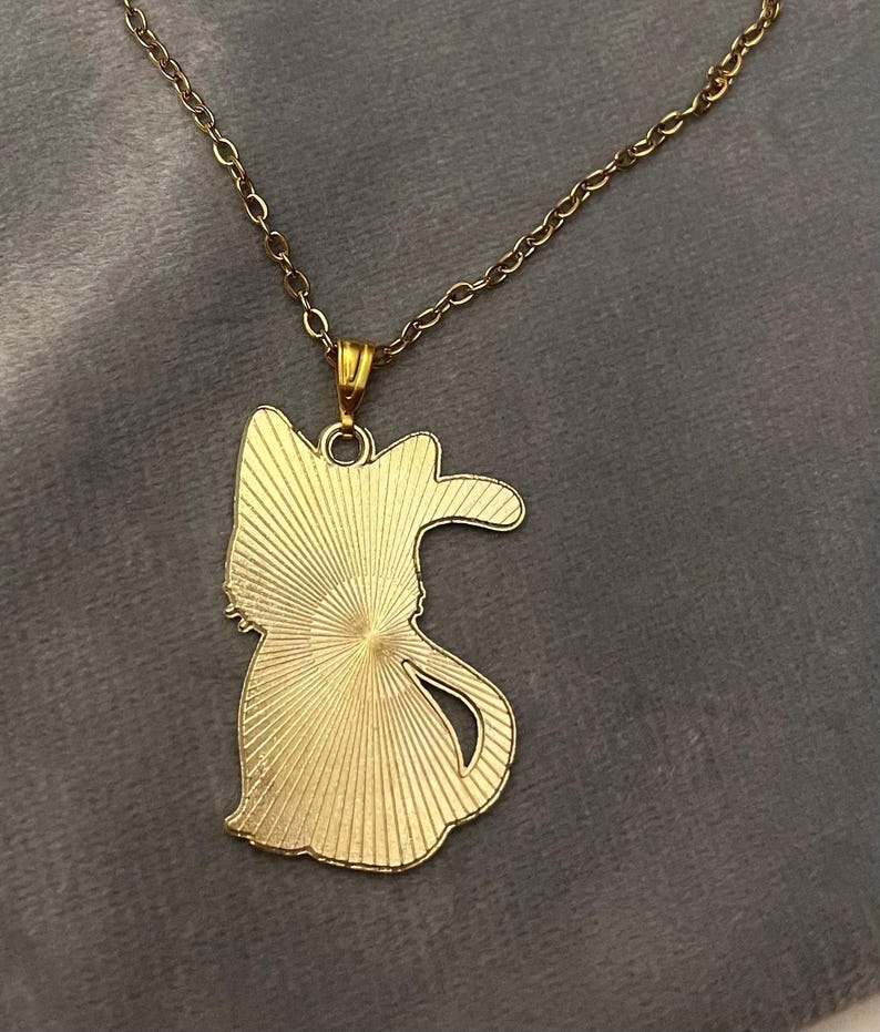 Op de afbeelding: Een gouden ketting met een hanger in de vorm van een kat. De hanger heeft een zonnestralenontwerp.