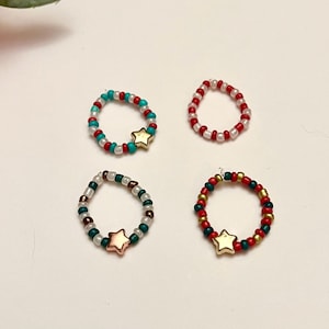 Könnte beinhalten: Vier Perlenringe mit Sternanhängern. Die Ringe sind aus roten, weißen, grünen und türkisfarbenen Perlen gefertigt.