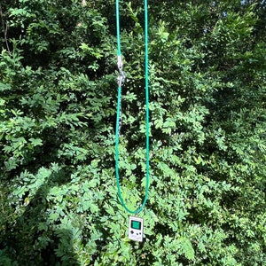 May include: A green cord necklace with a silver clasp and a pendant shaped like a vintage handheld video game console.