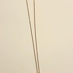 Op de afbeelding: Een gouden ketting met een zwarte kat hanger. De kat heeft roze oren en een halve maan op zijn voorhoofd. De ogen van de kat zijn oranje met een gele ster in elk oog.