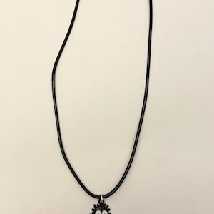 May include: Black cord necklace with a charm featuring a black soot sprite with white eyes and a pink tongue. The necklace has a silver-colored clasp and is displayed against a white background.