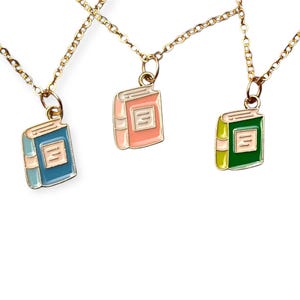 Op de afbeelding: Drie goudkleurige kettingkettingen, elk met een hanger in de vorm van een klein boek. De boekenhangers zijn blauw, roze en groen, met witte en gouden accenten. De boeken hebben een eenvoudig ontwerp.