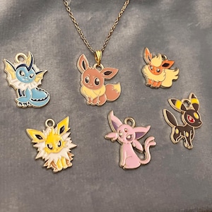 Può includere: Una collana dorata con un ciondolo raffigurante il personaggio Eevee marrone e crema. Intorno al ciondolo ci sono sei ciondoli smaltati colorati di vari personaggi Pokémon, tra cui Vaporeon, Flareon, Jolteon, Espeon e Umbreon.