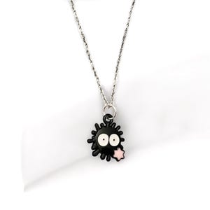 May include: A silver chain necklace with a black enamel pendant featuring a cartoon character with white eyes and a pink star.