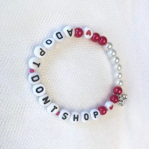 May include: White beaded bracelet with the words "I Don't Shop" and red heart beads.
