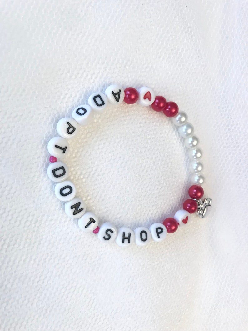 May include: White beaded bracelet with the words "I Don't Shop" and red heart beads.