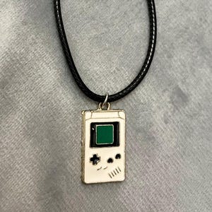 May include: A white and black game console pendant necklace with a green screen on a black cord.