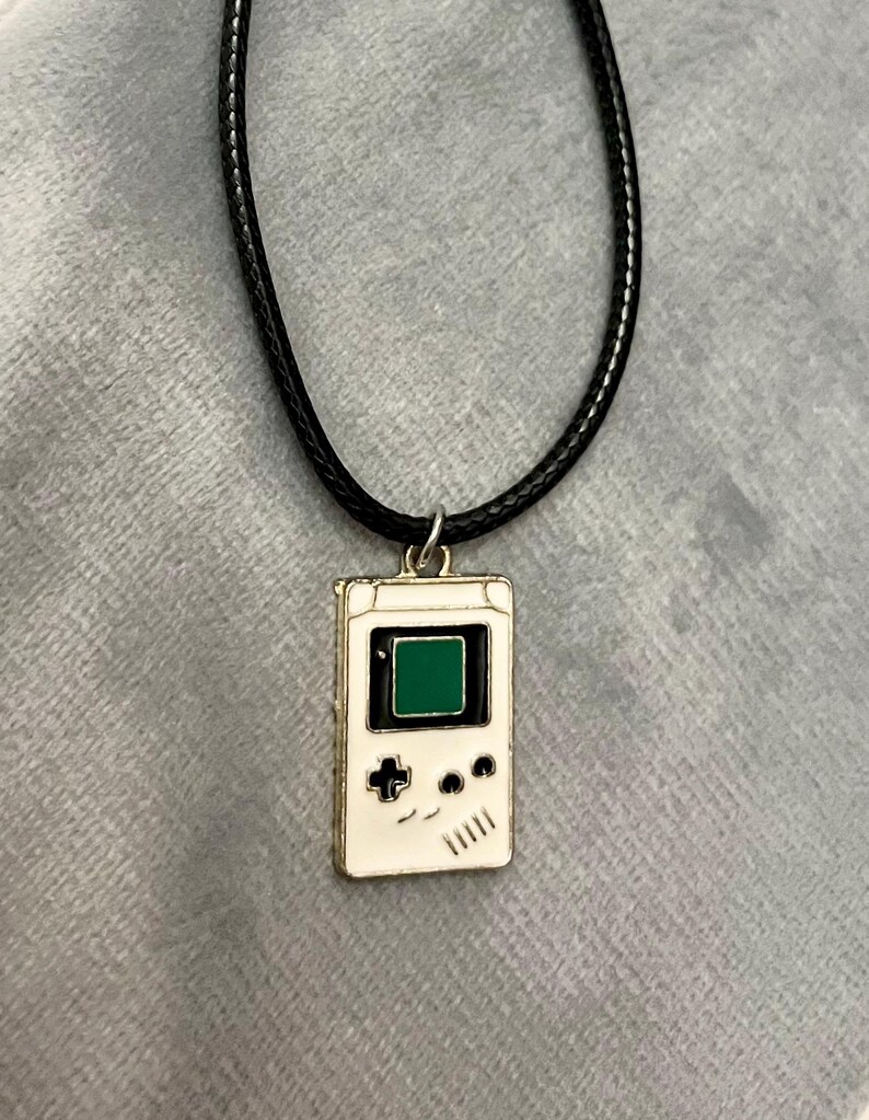 May include: A white and black game console pendant necklace with a green screen on a black cord.