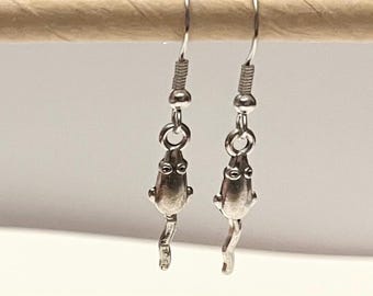 May include: Silver dangle earrings featuring a frog design. The frog is silver and has a long tail.