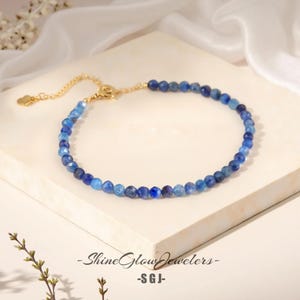 Op de afbeelding: Een delicate gouden ketting met een blauwe edelsteen kralenstreng. De kralen zijn in grootte aflopend, met de grotere kralen in het midden van de ketting. De ketting is verstelbaar en heeft een klein bedeltje aan het einde.