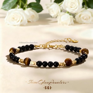 May include: A beaded bracelet featuring alternating black onyx beads and brown tiger eye beads, accented with small gold-toned metallic spacers. The bracelet includes a gold-toned chain extender with a lobster clasp and the text ShineGlowJewelers.