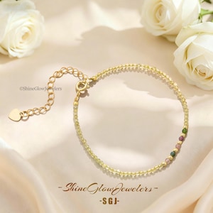 May include: A delicate gold chain bracelet featuring small, translucent yellow beads, accented with a few multicolored gemstone beads. The bracelet includes a gold extender chain finished with a small heart-shaped charm and the text ShineGlowJewelers.