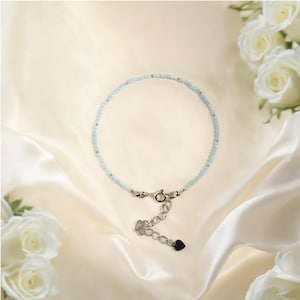 May include: A delicate light blue beaded bracelet with a silver clasp and a small silver heart charm.