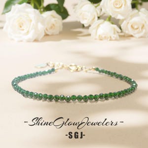 Peut inclure: Un bracelet délicat à perles vertes avec un fermoir doré. Le bracelet est composé de petites perles vertes facettées. Le fond présente des roses blanches et le texte "- Shine Glow Jewelers - SGJ -."