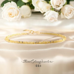 May include: A delicate gold necklace with small yellow beads and gold accents. The necklace is displayed on a white satin background.