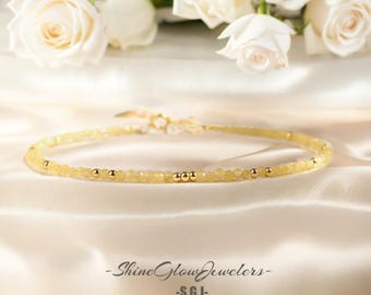 May include: A delicate gold necklace with small yellow beads and gold accents. The necklace is displayed on a white satin background.
