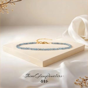 May include: A delicate blue gemstone necklace with a gold clasp. The necklace is displayed on a white surface.